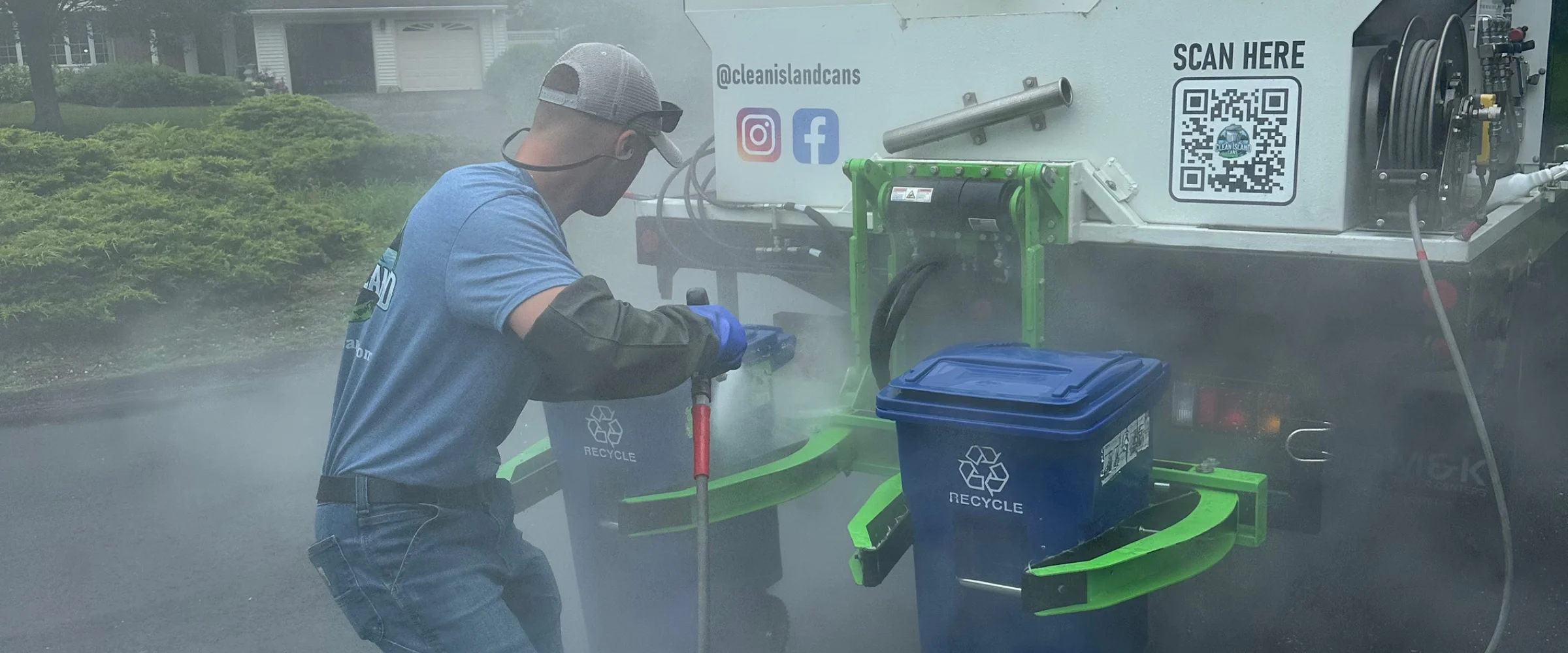 A row of two gray and three blue recycling bins with white symbols, lined up on an asphalt surface in sunlight.
