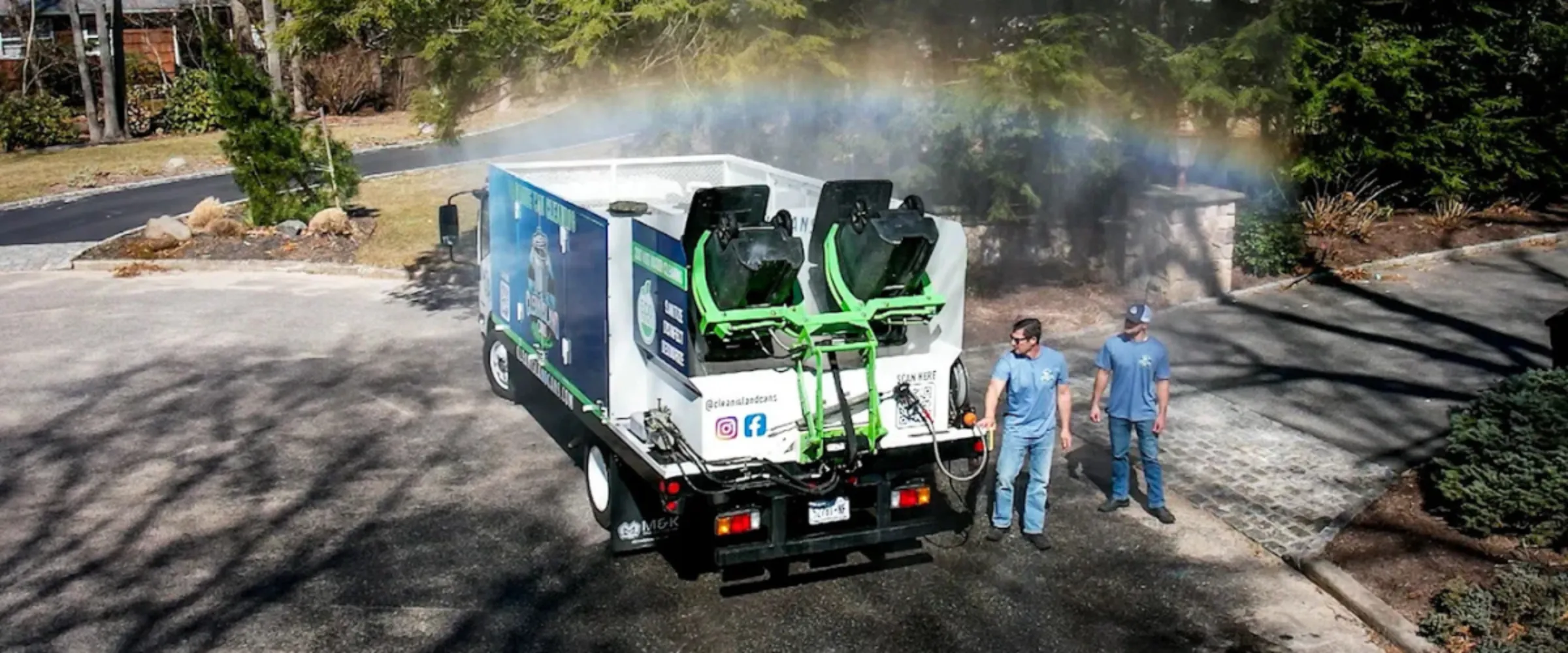 An overhead view of a specialized cleaning truck spraying mist, creating a rainbow, with two men standing nearby.
