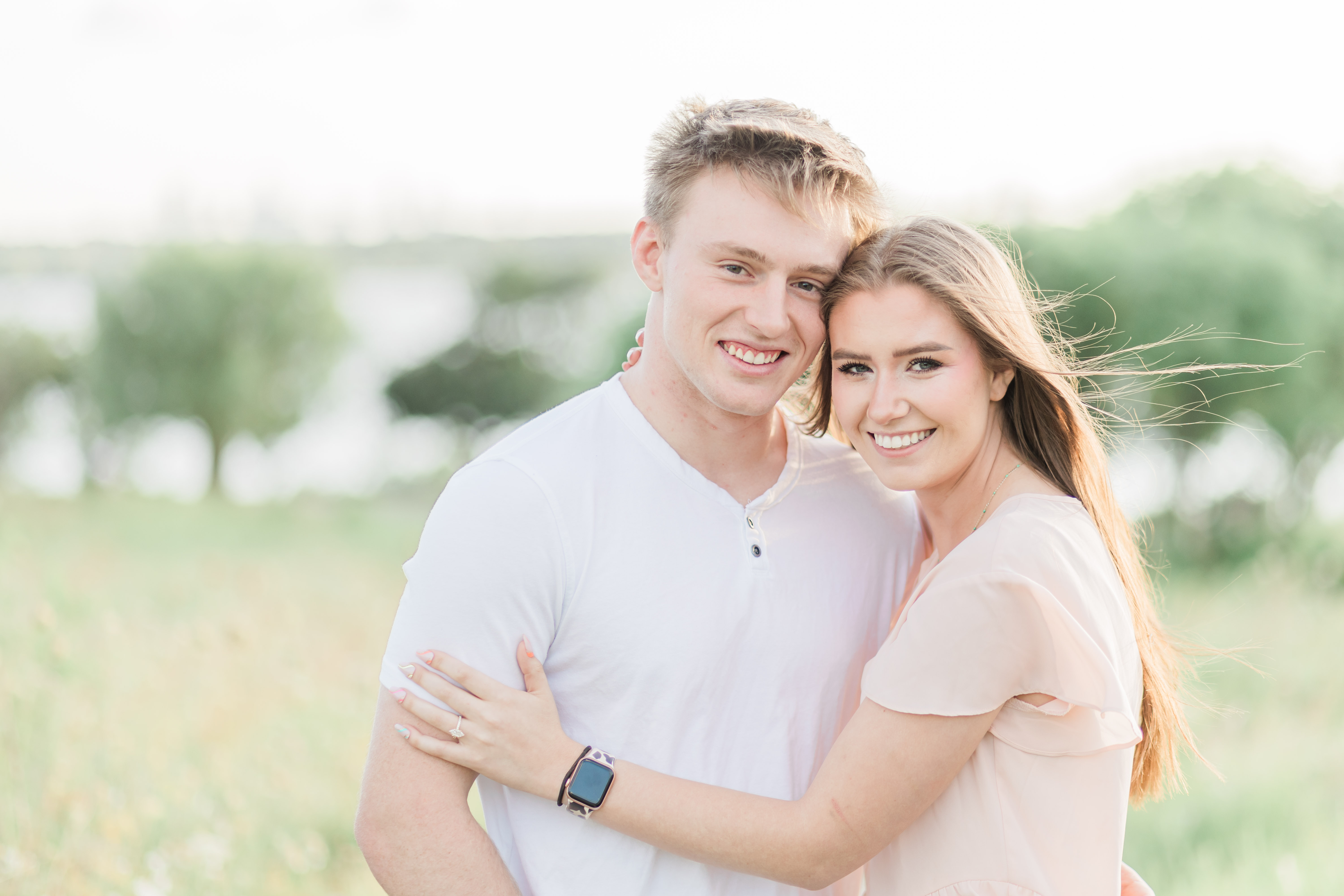 A young couple in an embrace on Winfrey Point with White Rock Lake in the background. Image captured by Arlene Stepanian Photography, a Dallas engagement and proposal photographer.