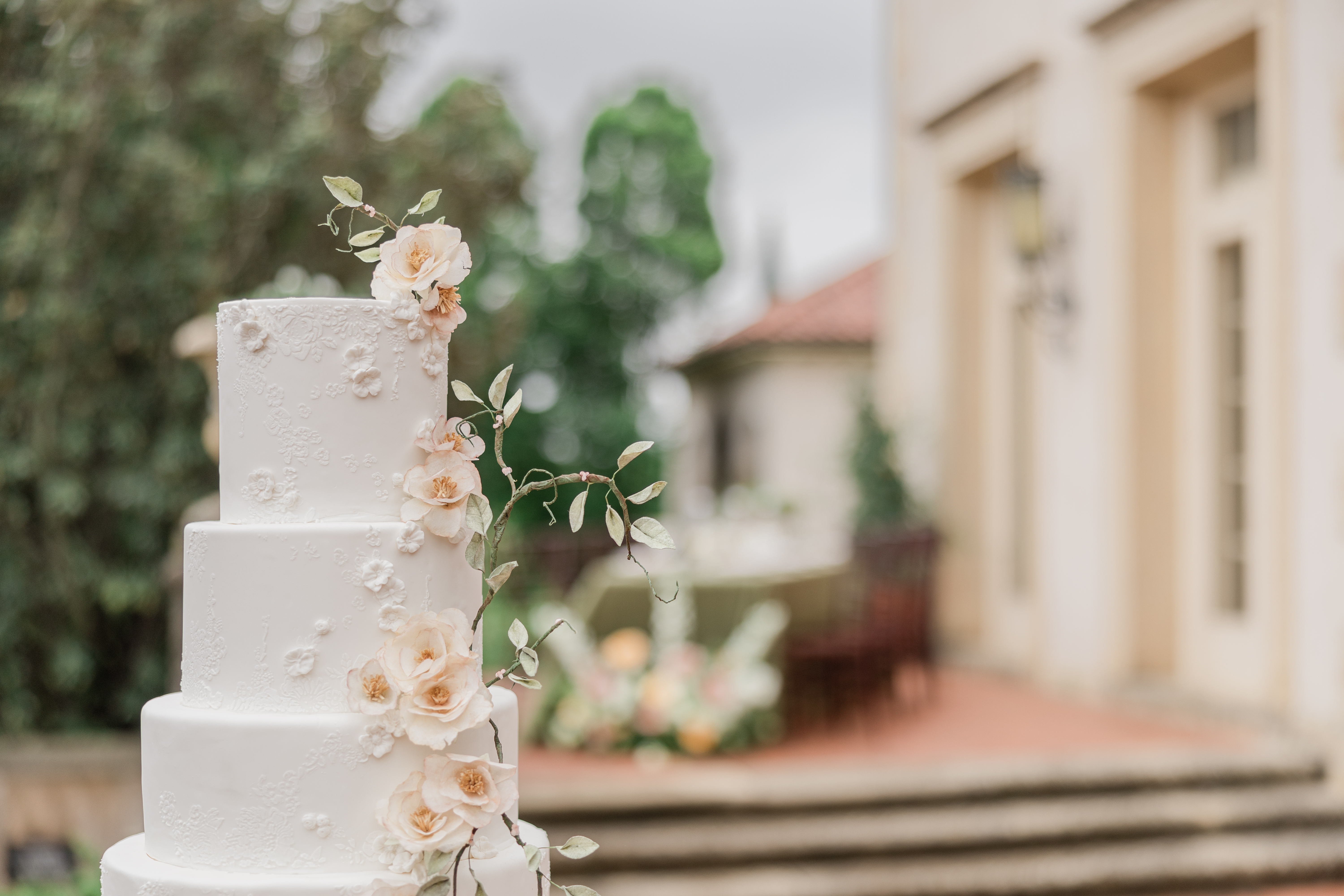 Image of a beautiful 4 tiered wedding cake set on a column outside on an Italian styled terrace at Philbrook Museum of Art in Tulsa, Ok. Captured y Arlene Stepanian Photogaphy.