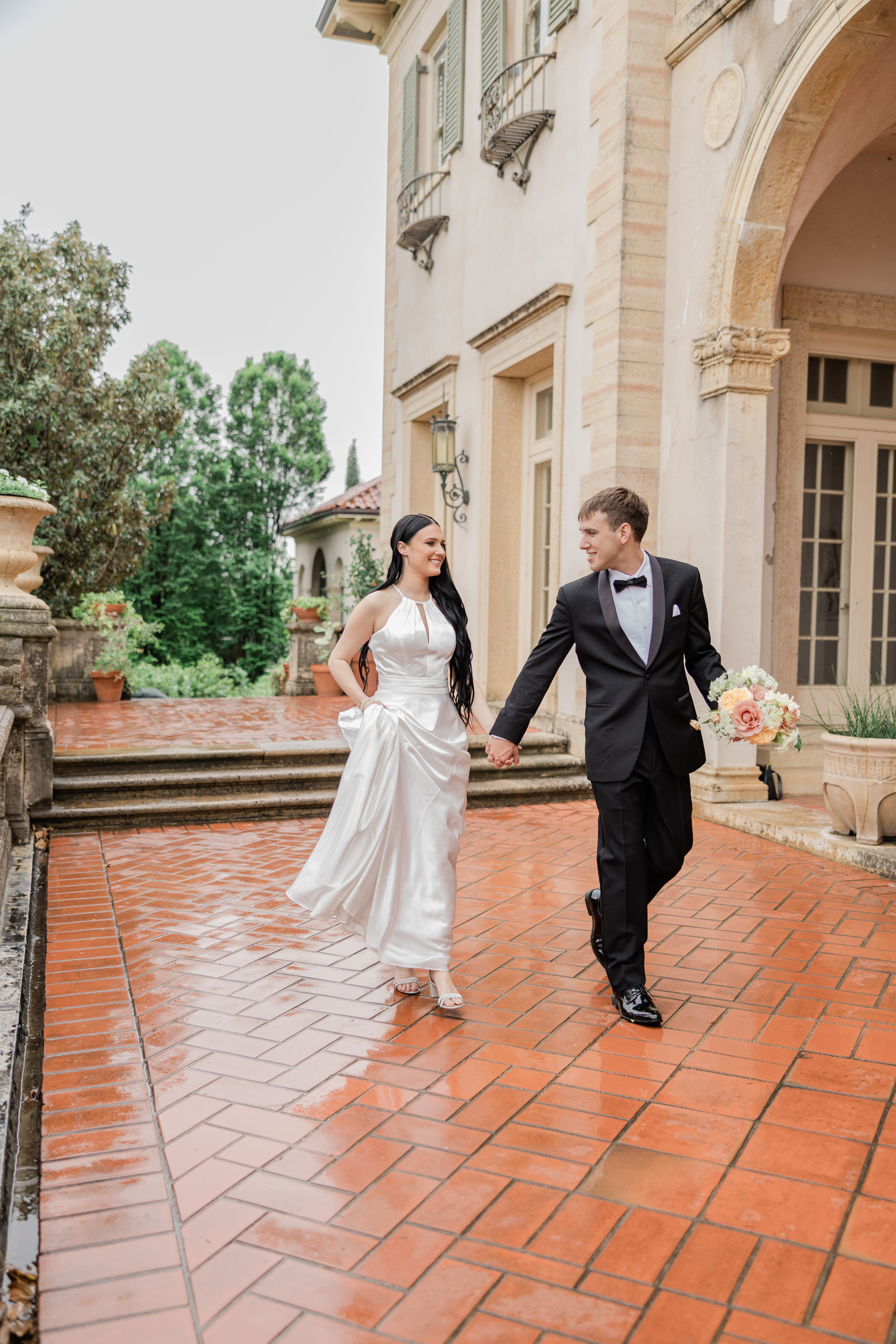 Bride is standing at bottom of curved staircase leaning over the handrail to kiss her groom at The Lone Star Mansion in Burleson Tx.