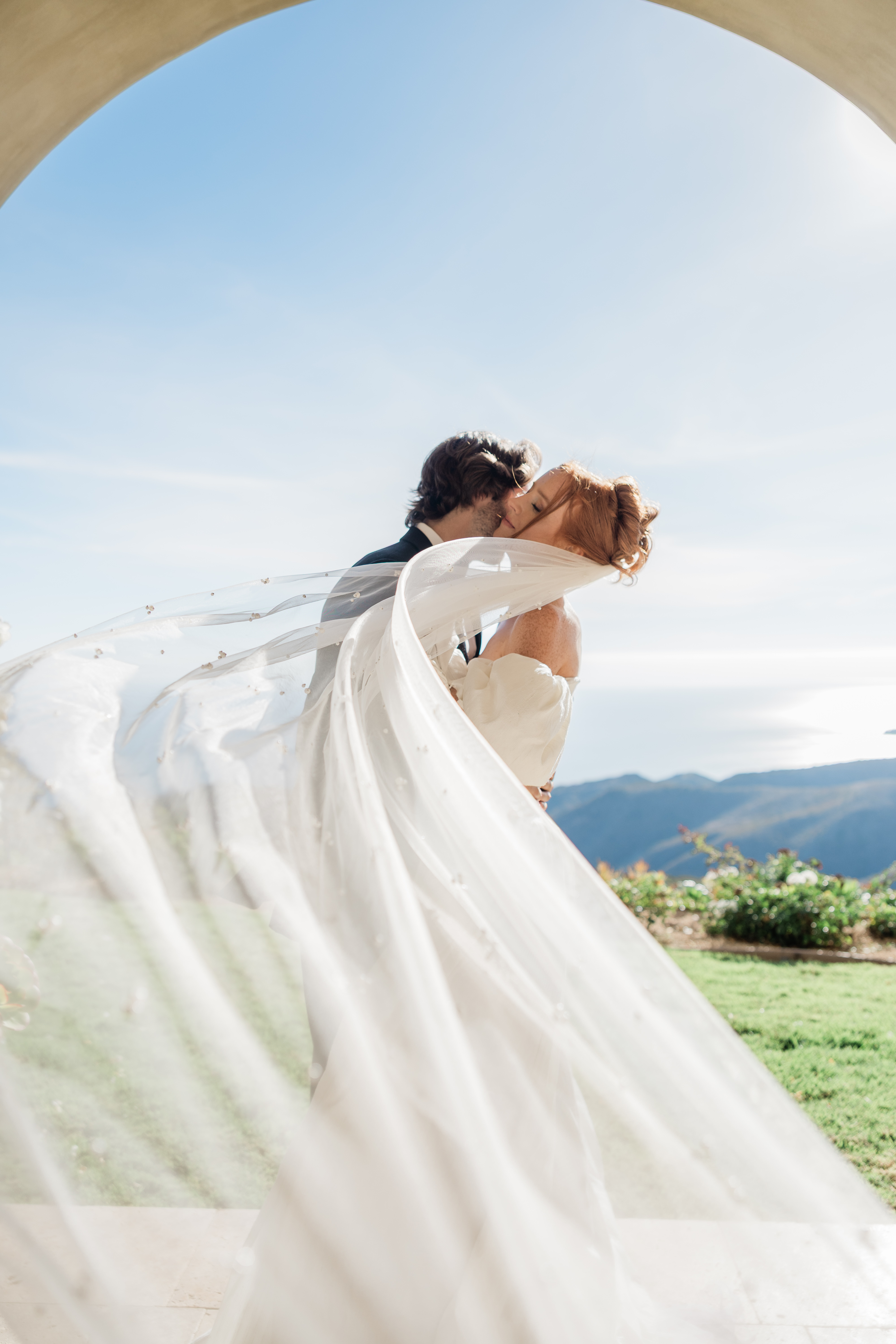 Editorial bride and groom portrait with flowing veil, mountain views, and romantic wedding-day movement.