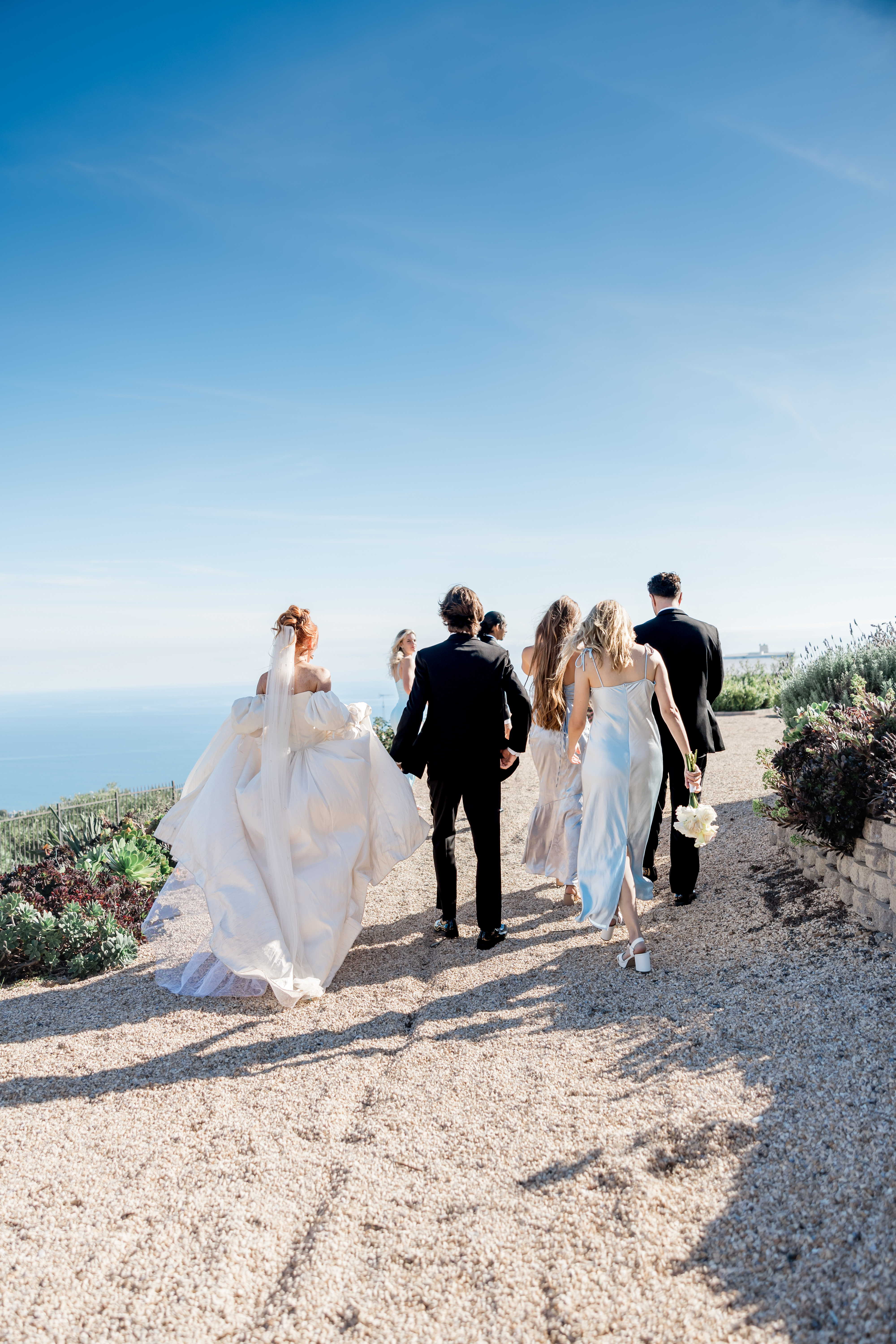 Bride and wedding party walking along a scenic coastal path in a documentary Dallas wedding photography moment.