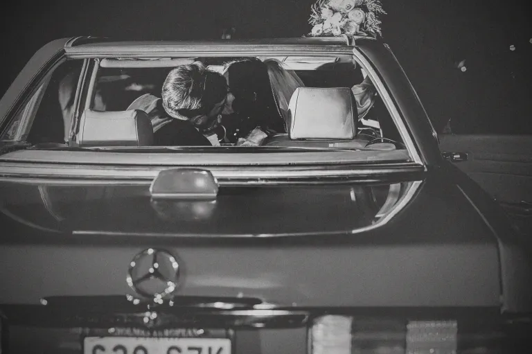 Dallas Wedding Photographer capturing a black and white vintage getaway car kiss after the wedding reception.