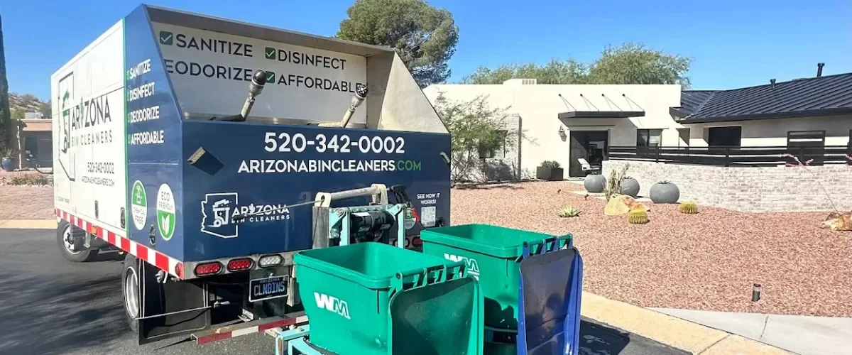 A green garbage truck with a bin attached to its side, and a worker rolling another bin into position.