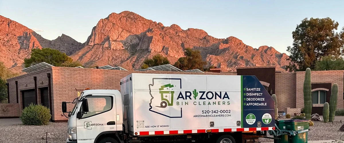 A white Arizona Bin Cleaners truck parked in front of houses with large mountains in the background at sunset.