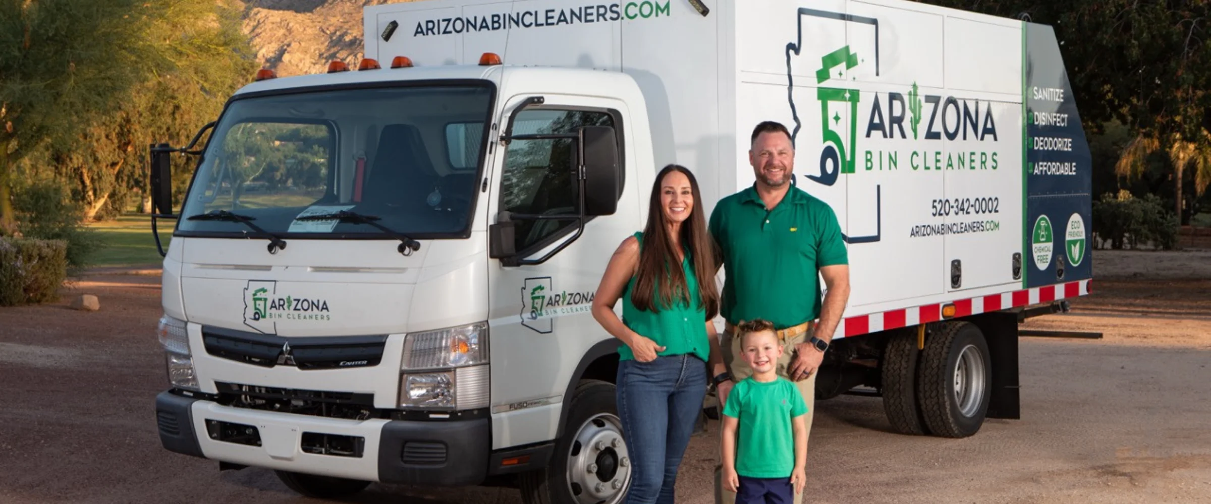 A family of three, parents and young son, smiling in front of their white Arizona Bin Cleaners truck.