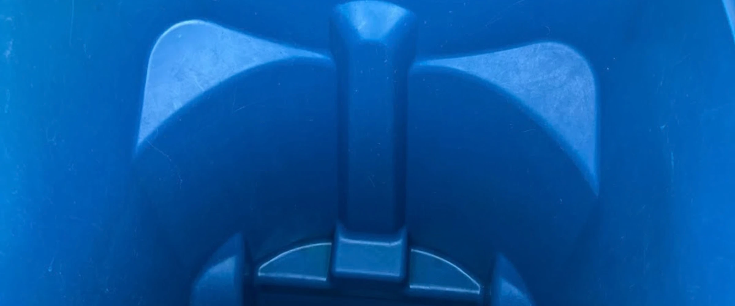 A top-down view inside a clean, empty blue plastic bin or wheeled trash can with a small puddle of water at the bottom. A top-down view inside a clean, empty blue plastic bin or wheeled trash can with a small puddle of water at the bottom.
