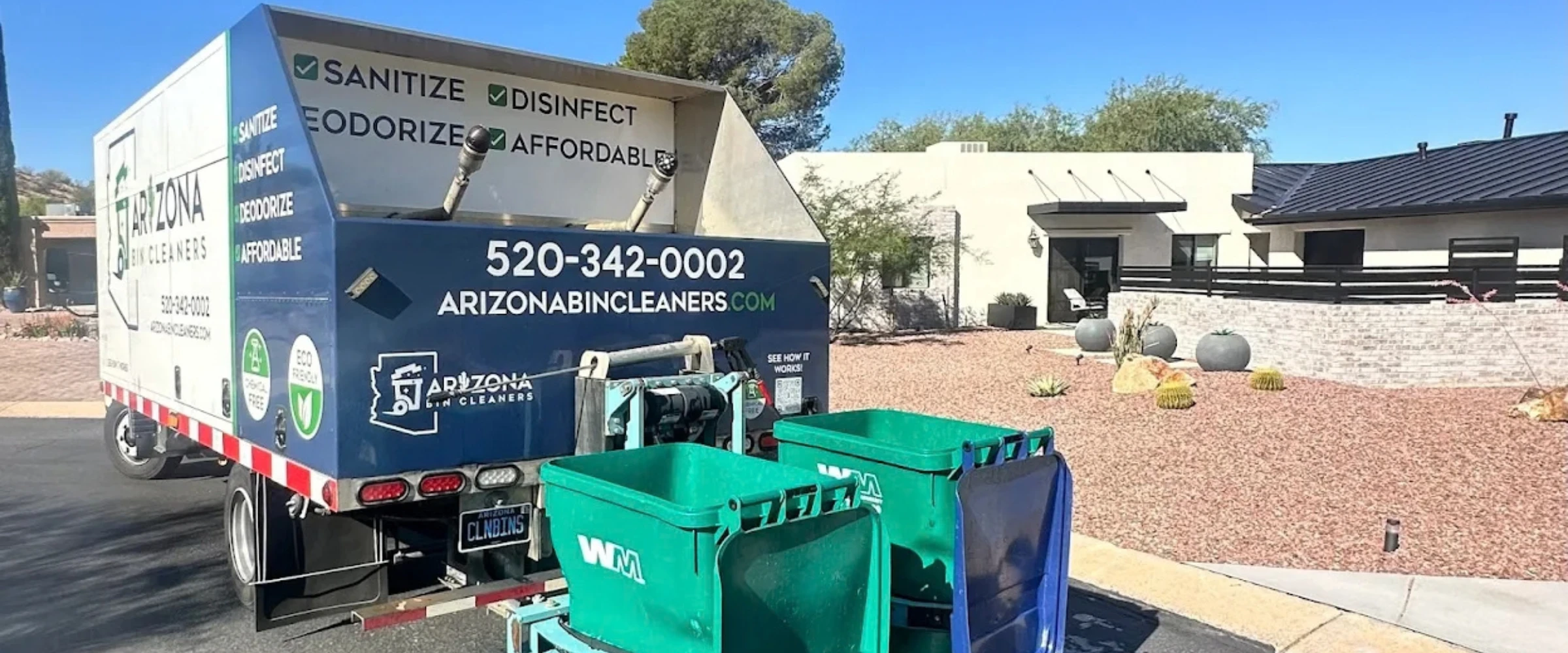 A blue and white Arizona Bin Cleaners truck with green bins attached, parked on a residential street with desert landscaping. A blue and white Arizona Bin Cleaners truck with green bins attached, parked on a residential street with desert landscaping.