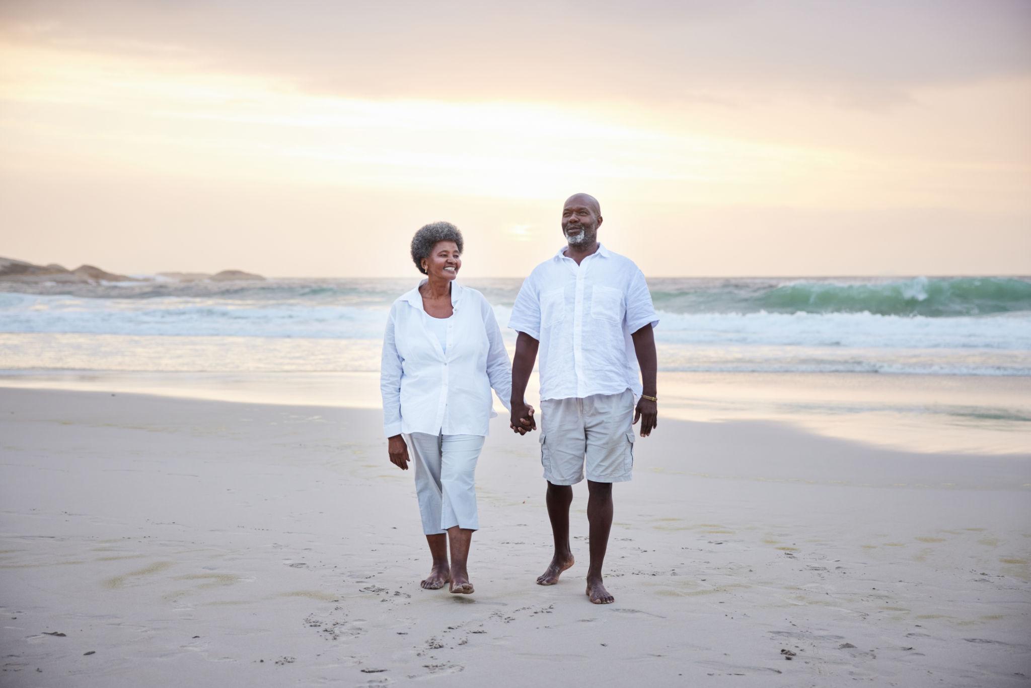 Smiling senior couple walking together on a sandy beach at sunset