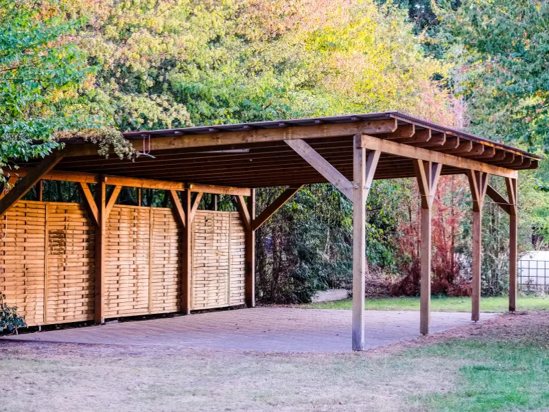 Freestanding wooden carport with slatted side panels in a backyard setting. Freestanding wooden carport with slatted side panels in a backyard setting.