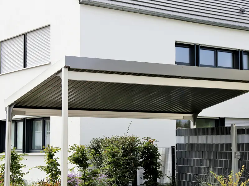 Attached metal carport with corrugated roof panels beside a two-story home. Attached metal carport with corrugated roof panels beside a two-story home.
