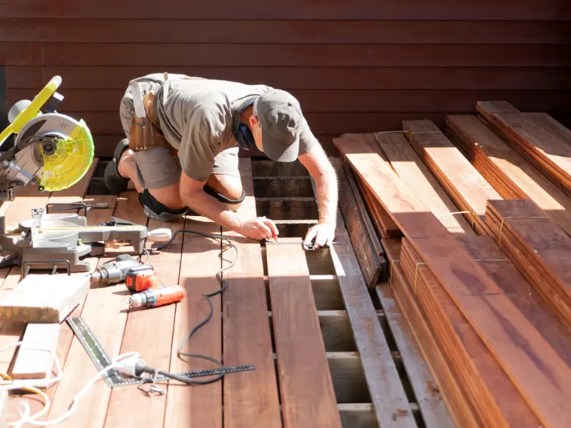 Contractor measuring deck boards next to a miter saw during deck board replacement. Contractor measuring deck boards next to a miter saw during deck board replacement.