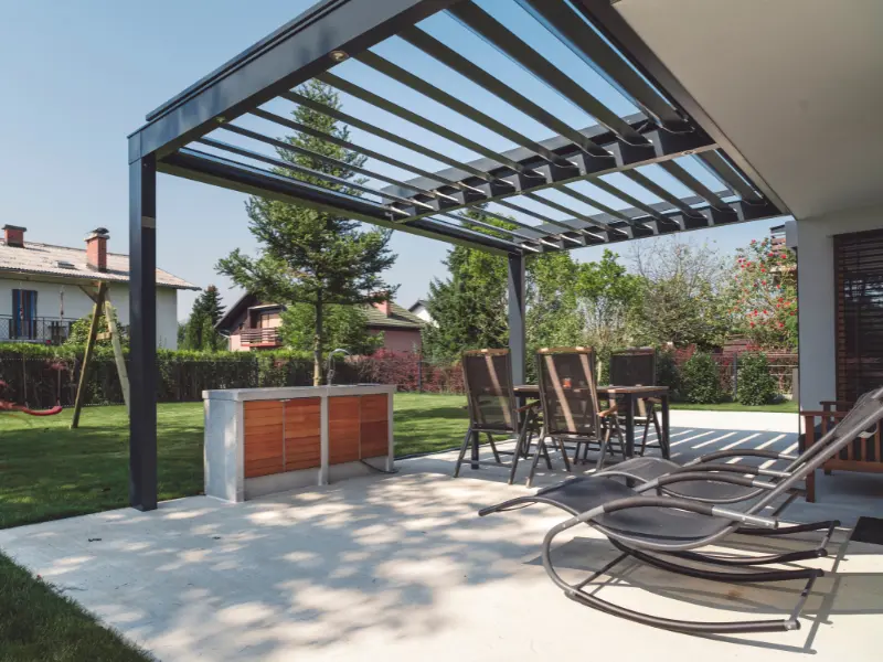 Custom aluminum pergola with open rafters shading a backyard patio with seating and outdoor kitchen.