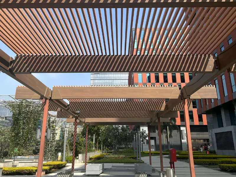 Custom wood pergola with slatted rafters providing shade in an outdoor plaza setting.