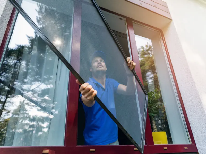 Installer fitting a mesh screen panel into a window frame as part of a screen room build.