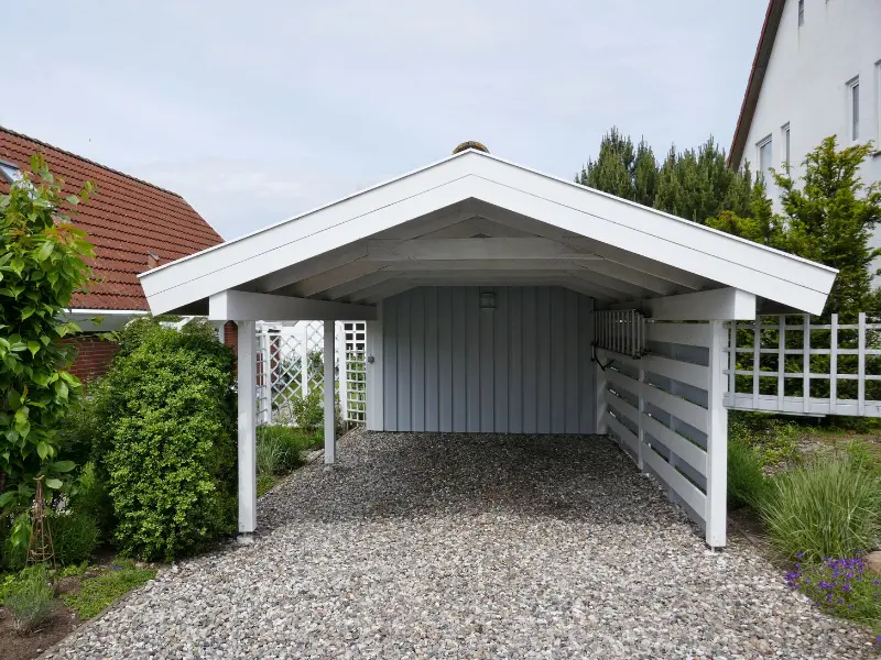 White gable-roof carport with an enclosed back wall over gravel.