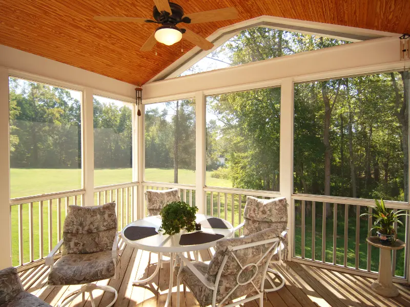 Screened porch with wood ceiling fan and wicker furniture overlooking yard. Screened porch with wood ceiling fan and wicker furniture overlooking yard.