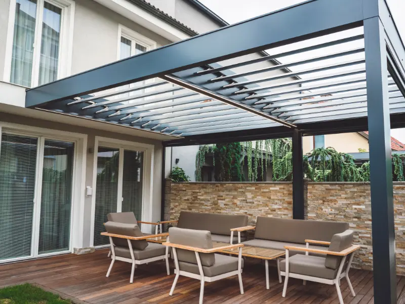 Motorised louvered pergola over a backyard patio with lounge seating.