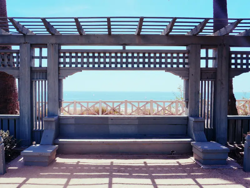 Open rafter wooden pergola framing a bench with an ocean view.