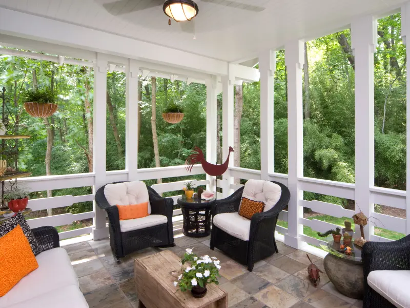 Screened in porch with wicker furniture and wooded backyard view.