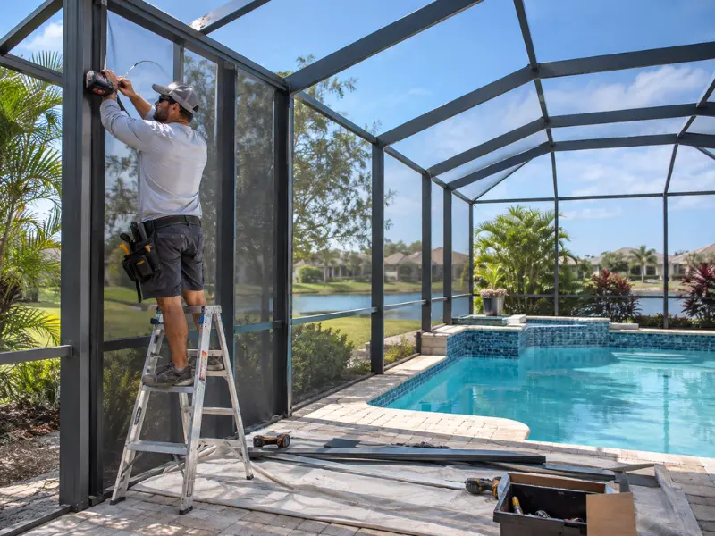 Technician installing pool screen enclosure mesh panels on an aluminum frame beside an in-ground pool.