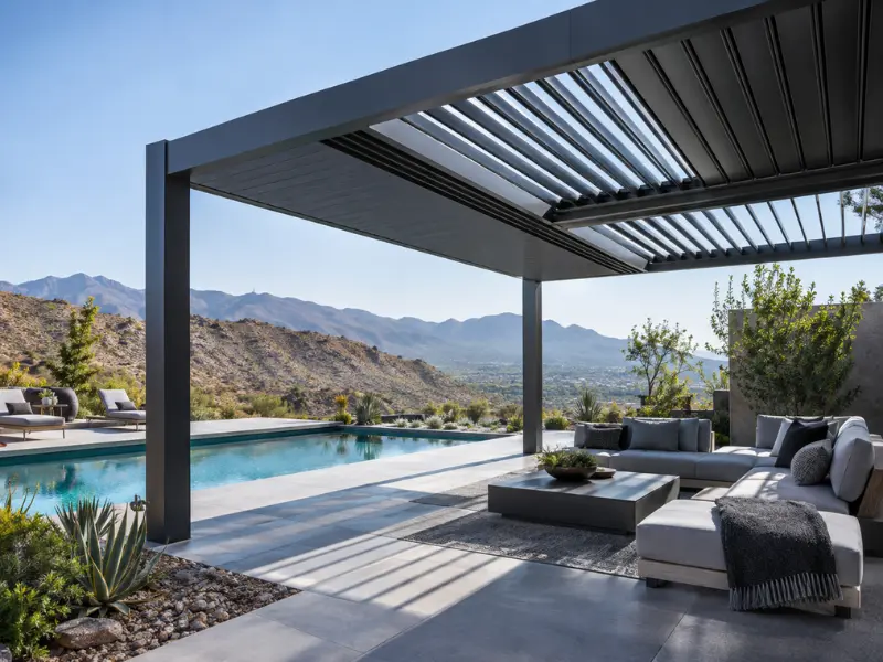 Modern aluminum louvered pergola patio cover shading an outdoor sofa and pool deck with mountain views in the background. Modern aluminum louvered pergola patio cover shading an outdoor sofa and pool deck with mountain views in the background.