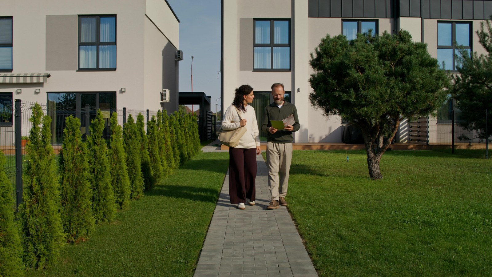 Two people walking a path beside a building, looking at a tablet together