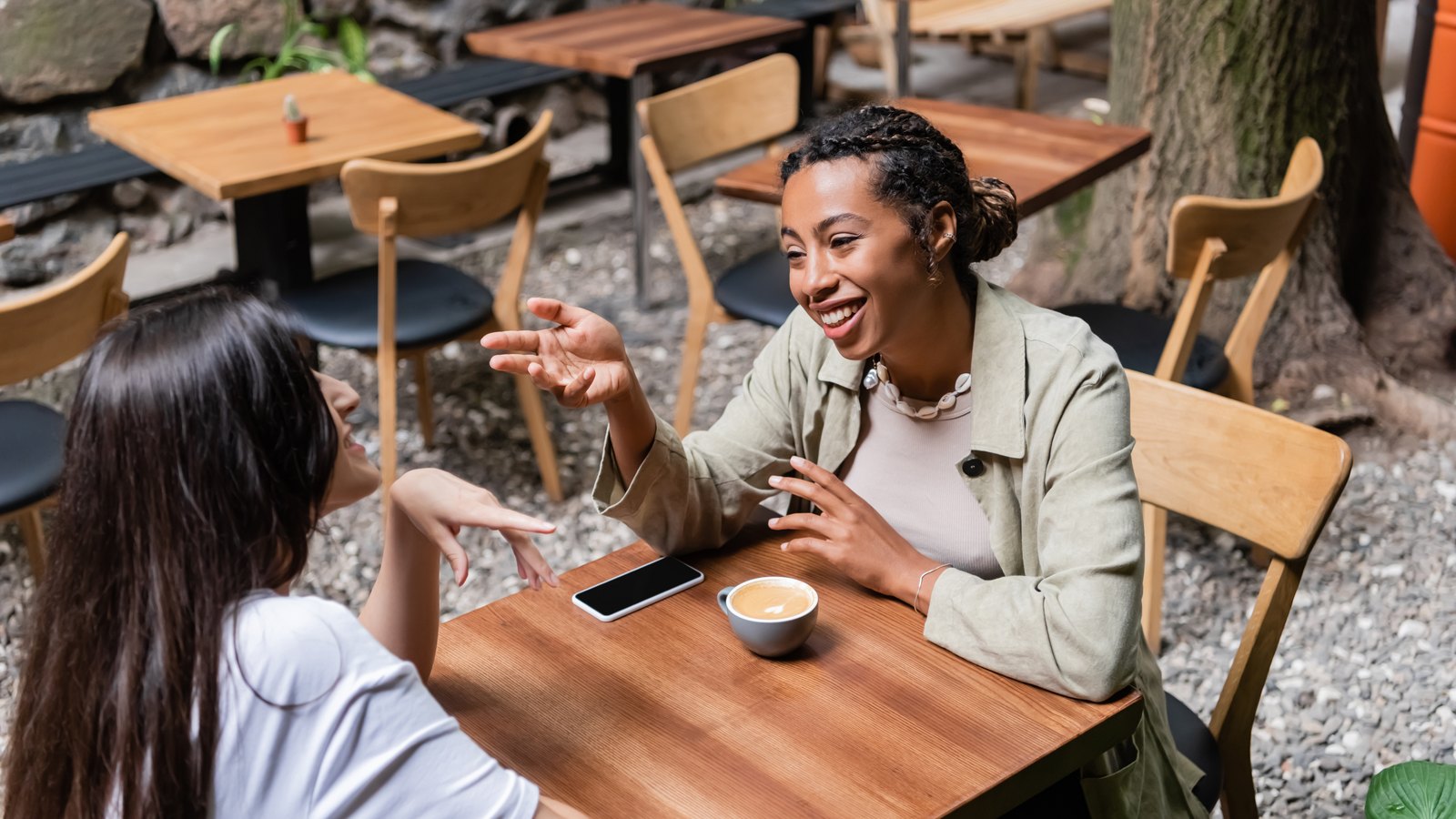 Two women laughing and talking over coffee at an outdoor cafe table