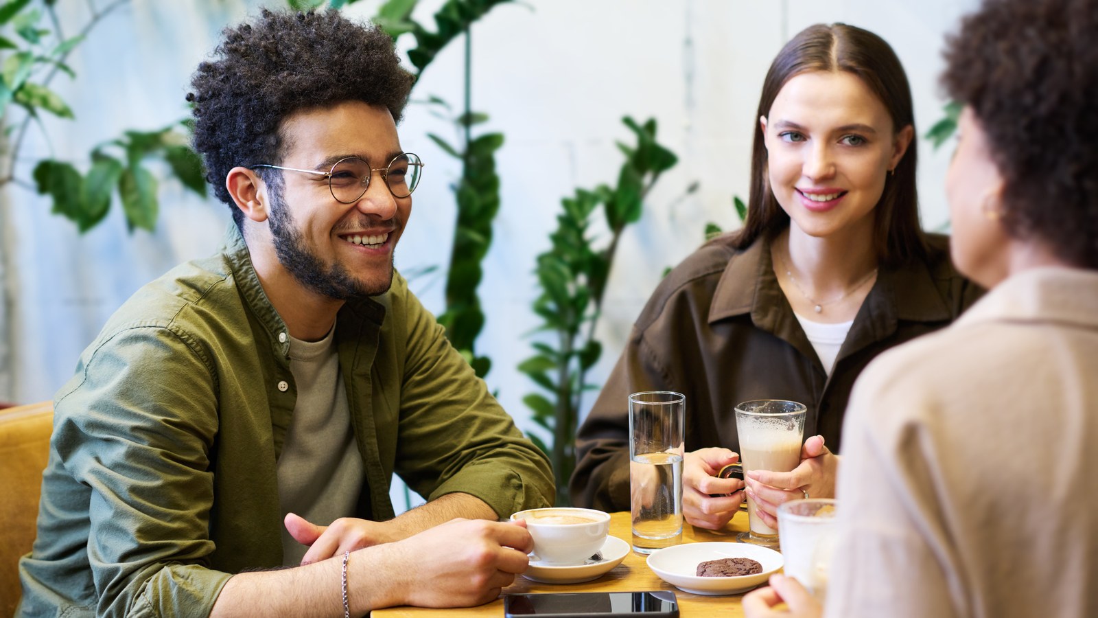Three friends talking and laughing over coffee at a cafe table