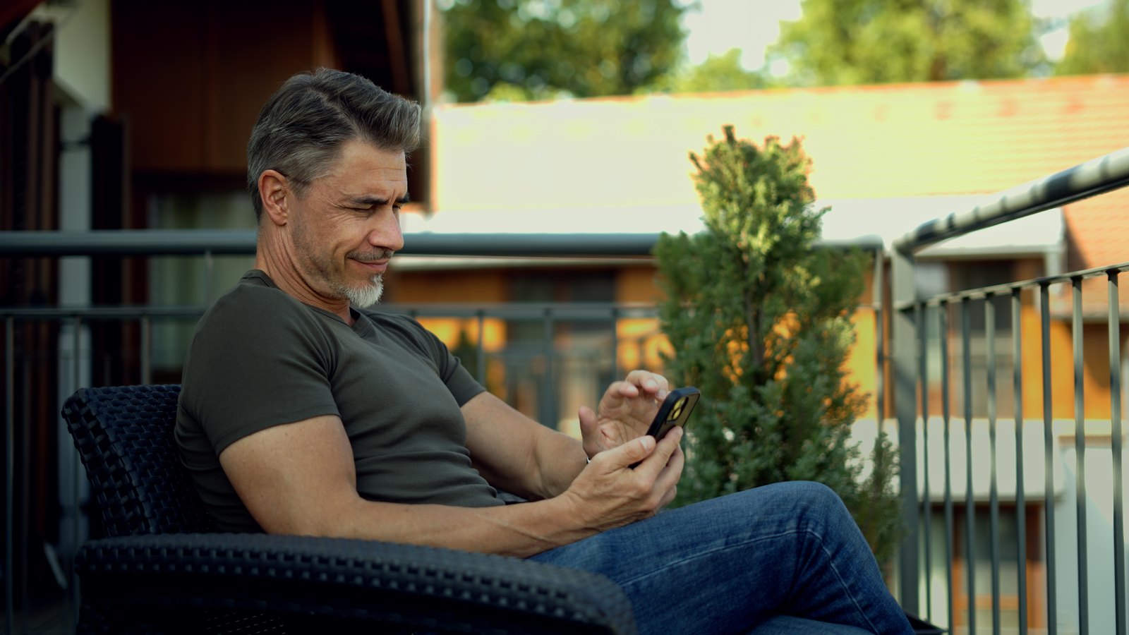 A man relaxing on a sunny balcony, reading a message on his phone