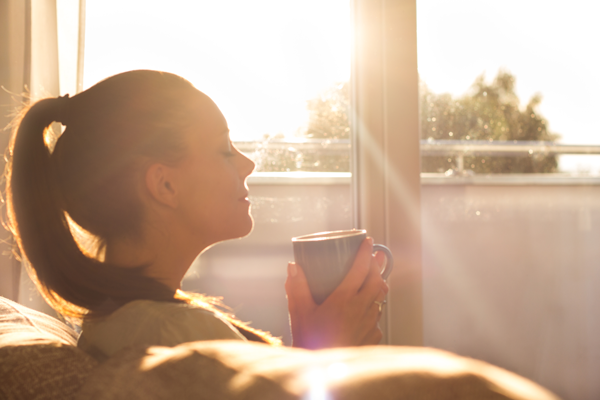 Woman holding a cup of coffee in the sun — a moment of awakening