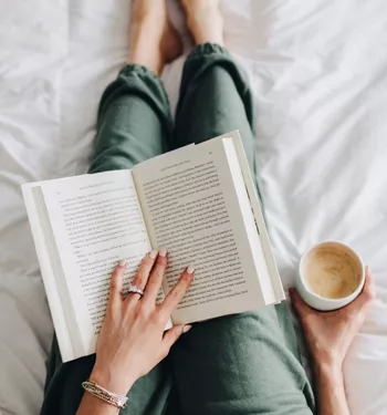 Overhead view of a woman holding a book and a cup of coffee in her lap