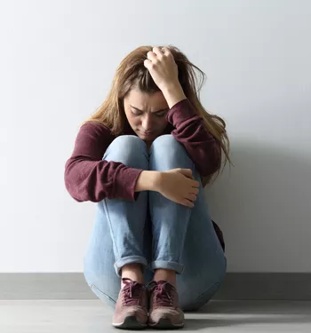 Woman sitting on the floor with knees pulled in, holding her head in visible overwhelm
