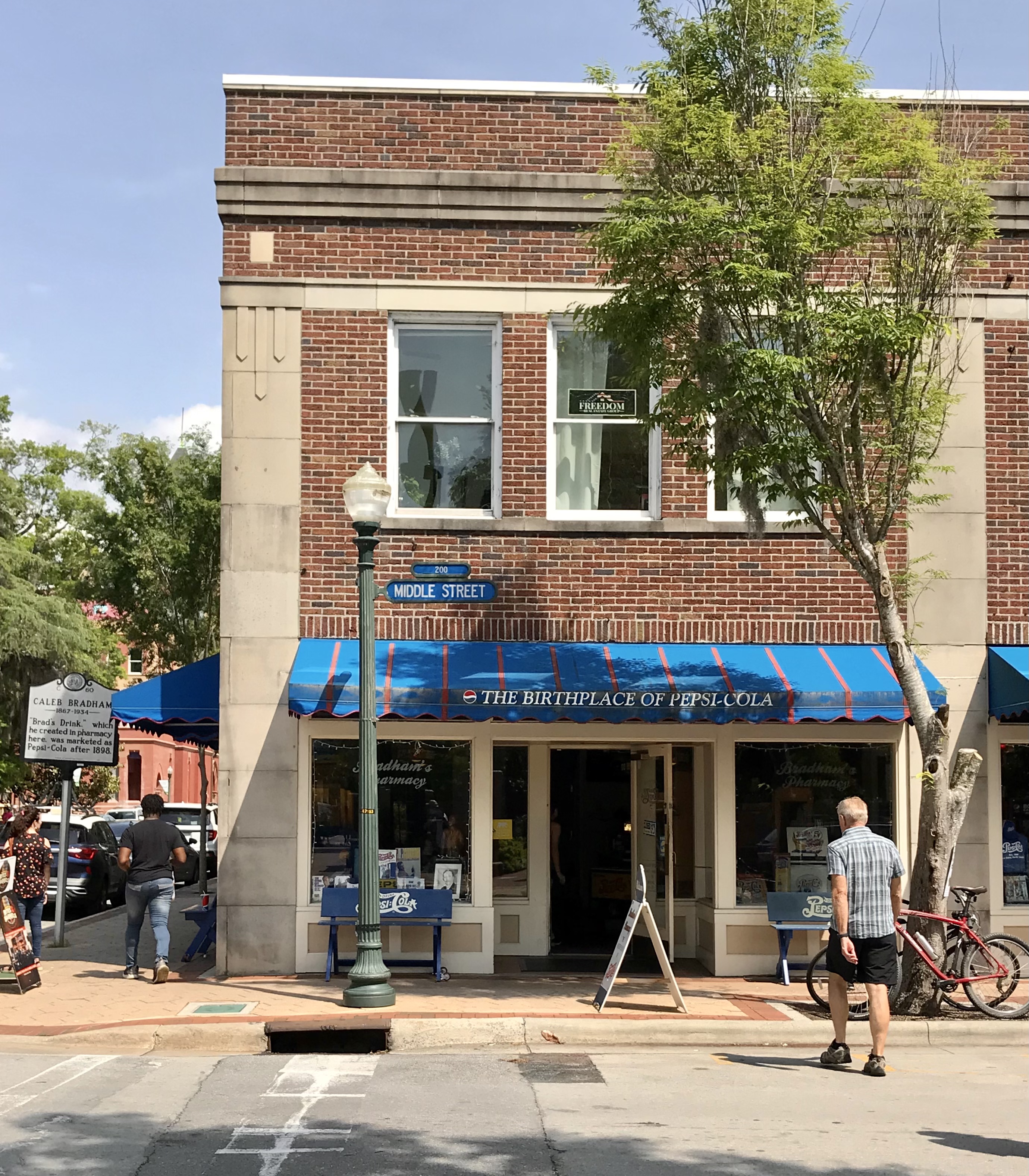 The brick storefront of The Birthplace of Pepsi-Cola on Middle Street, with a blue awning.