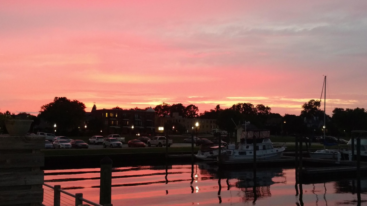 Pink sunset over boats moored at a New Bern marina, with the downtown waterfront across the water.