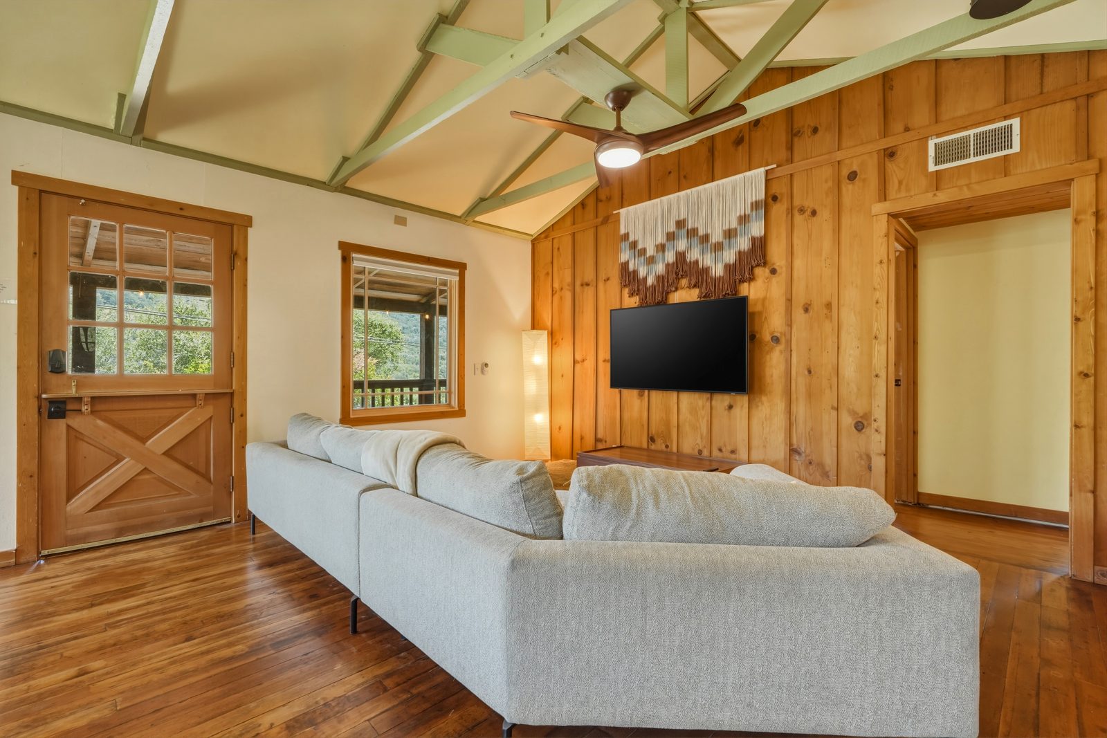 Wood-paneled cabin living room with vaulted beams and a sectional sofa