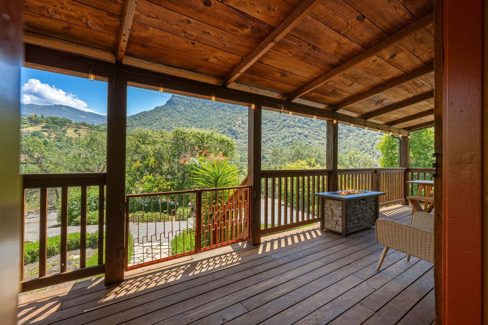 Covered deck with a fire table overlooking the Three Rivers foothills and mountains, at a short-term rental Lis manages