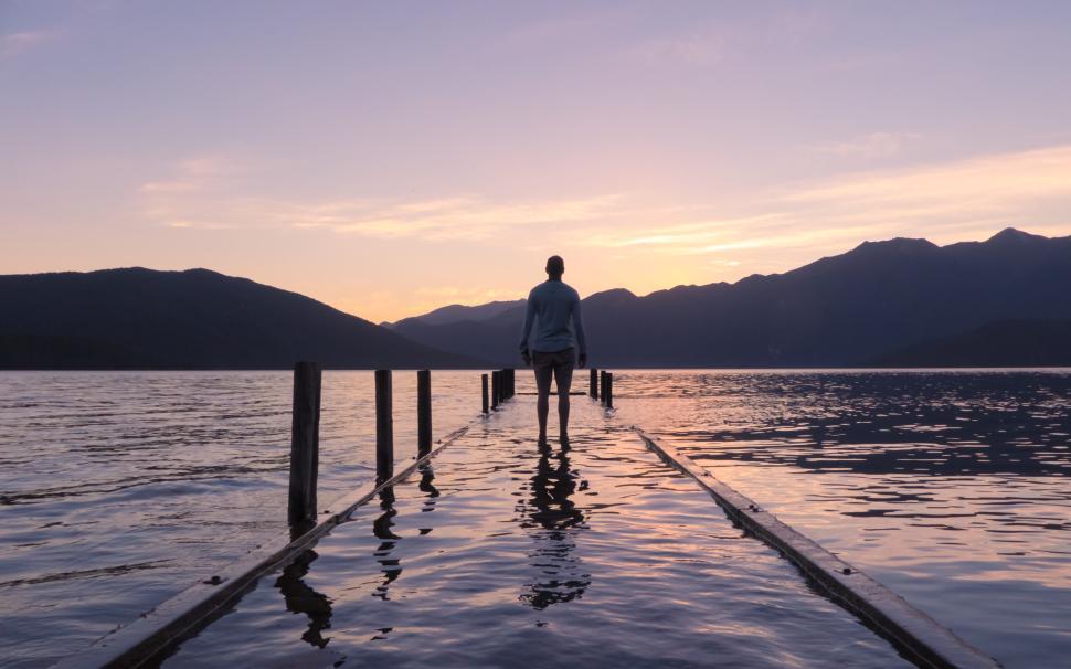 person standing on pier at sunrise over tranquil lake