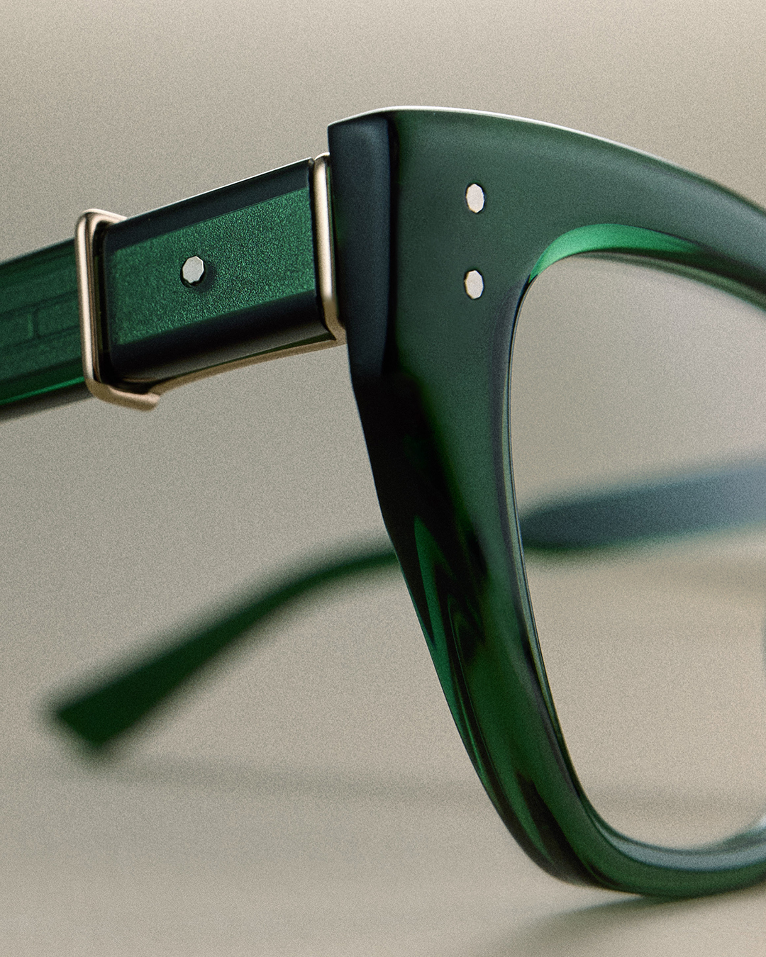 Close-up of a translucent emerald-green eyeglass frame featuring silver rivets and a polished metal hinge.
