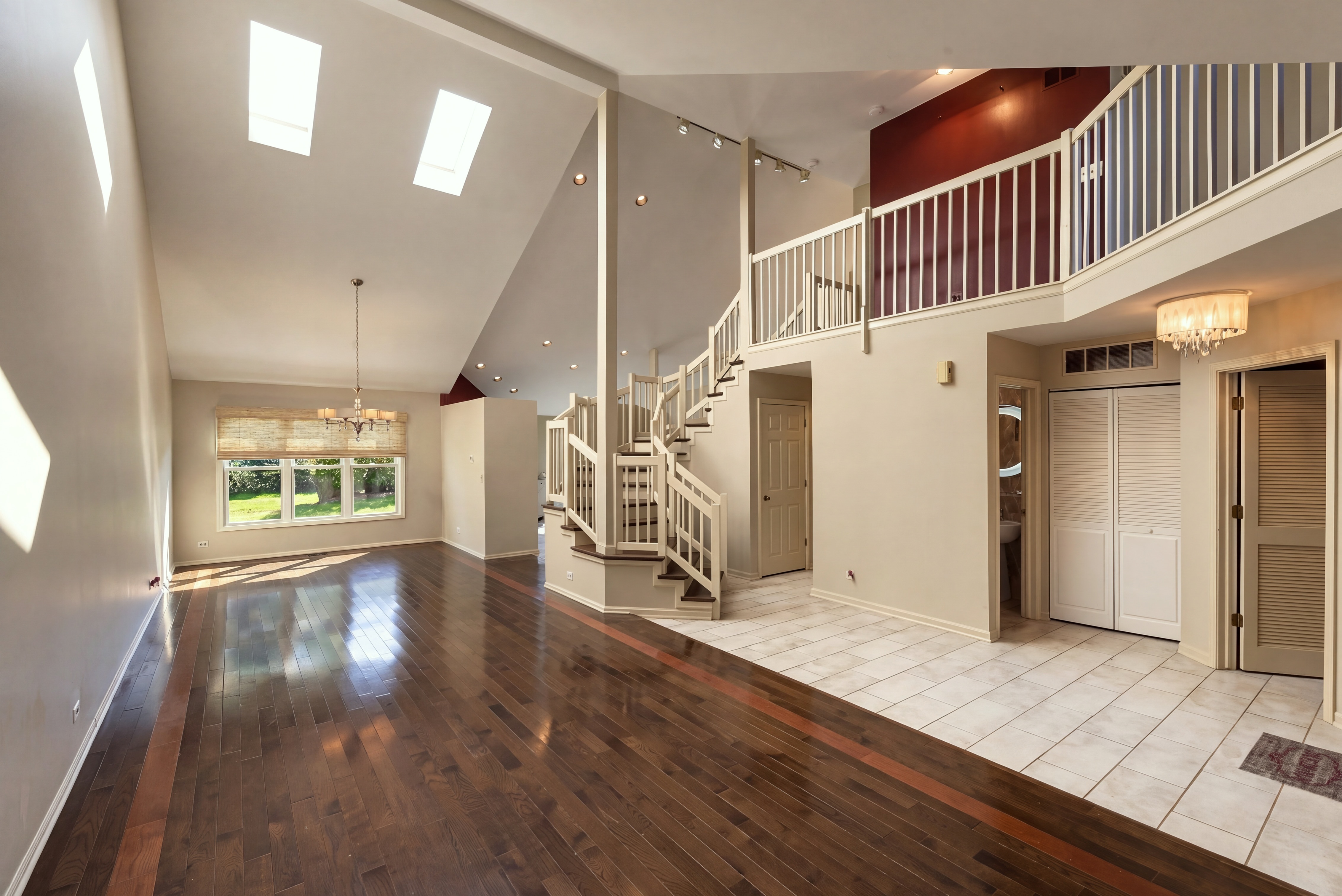 Open interior with skylights, hardwood flooring, and a staircase leading to an upper landing