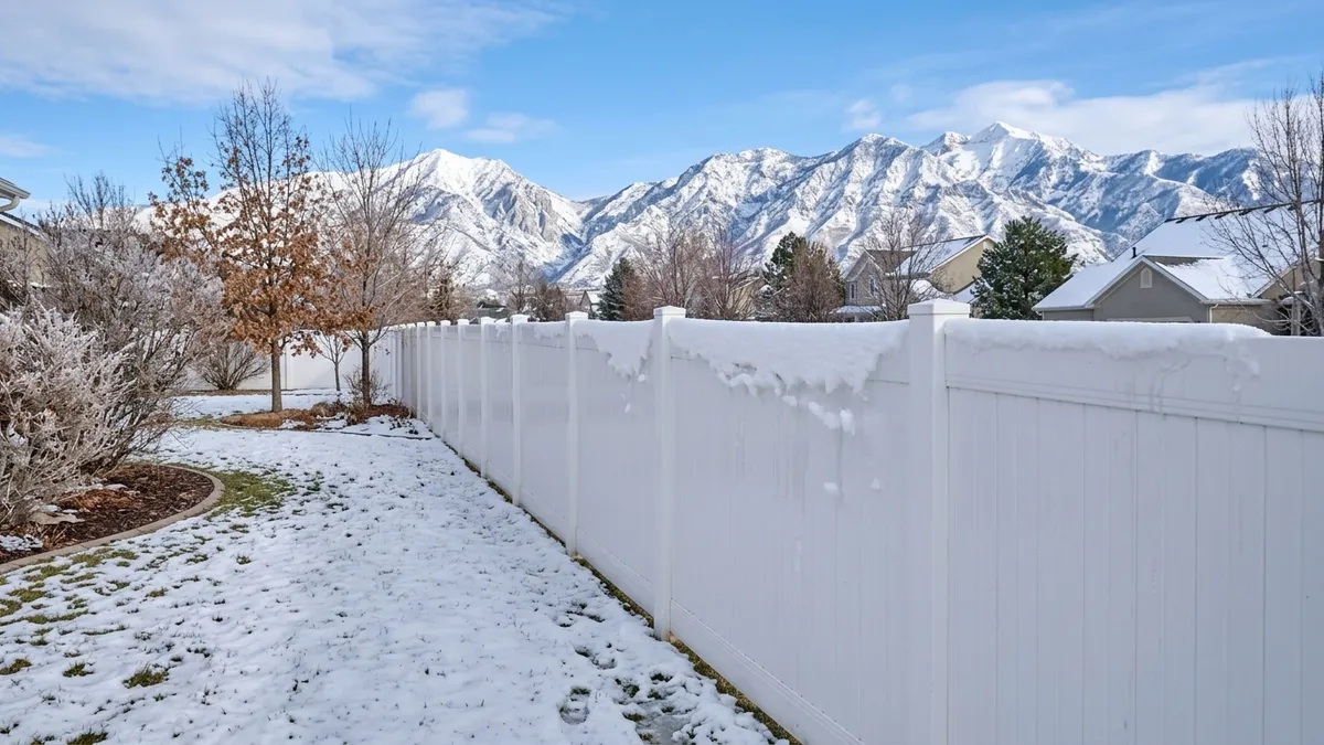White vinyl privacy fence shedding wet spring snow with snowy Wasatch peaks behind