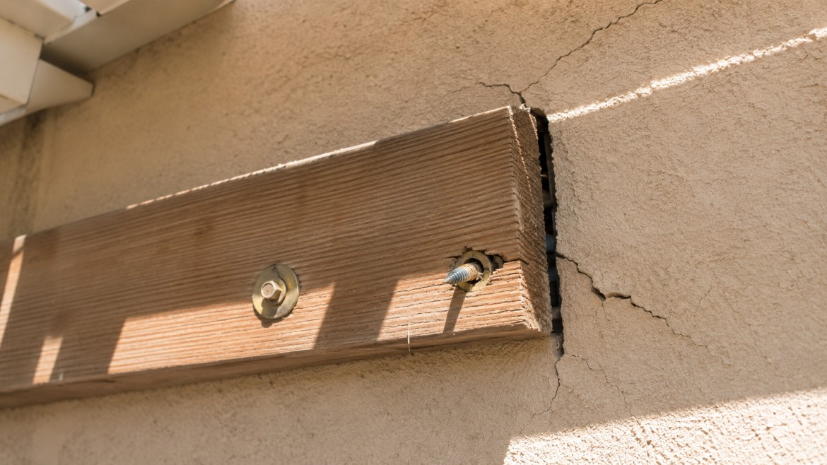 Patio cover ledger pulling away from a stucco wall where fasteners missed framing