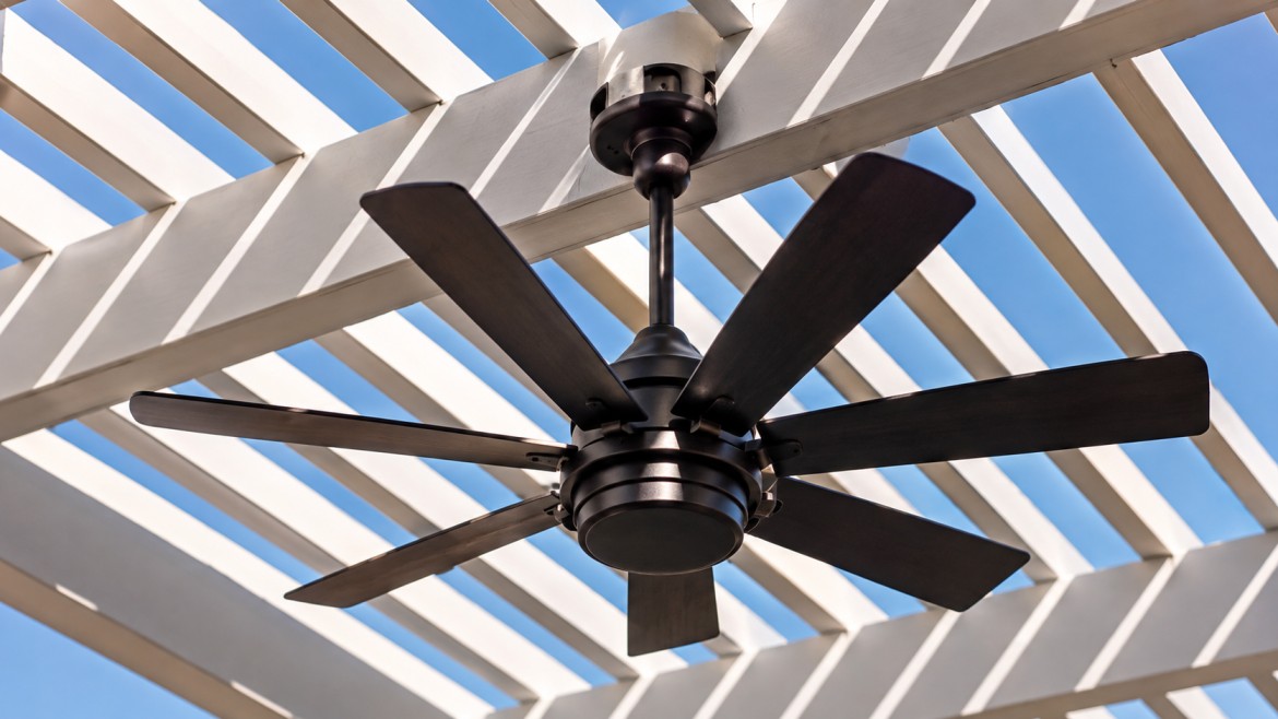 Wet-rated ceiling fan mounted beneath an open pergola roof with sunlight striping through