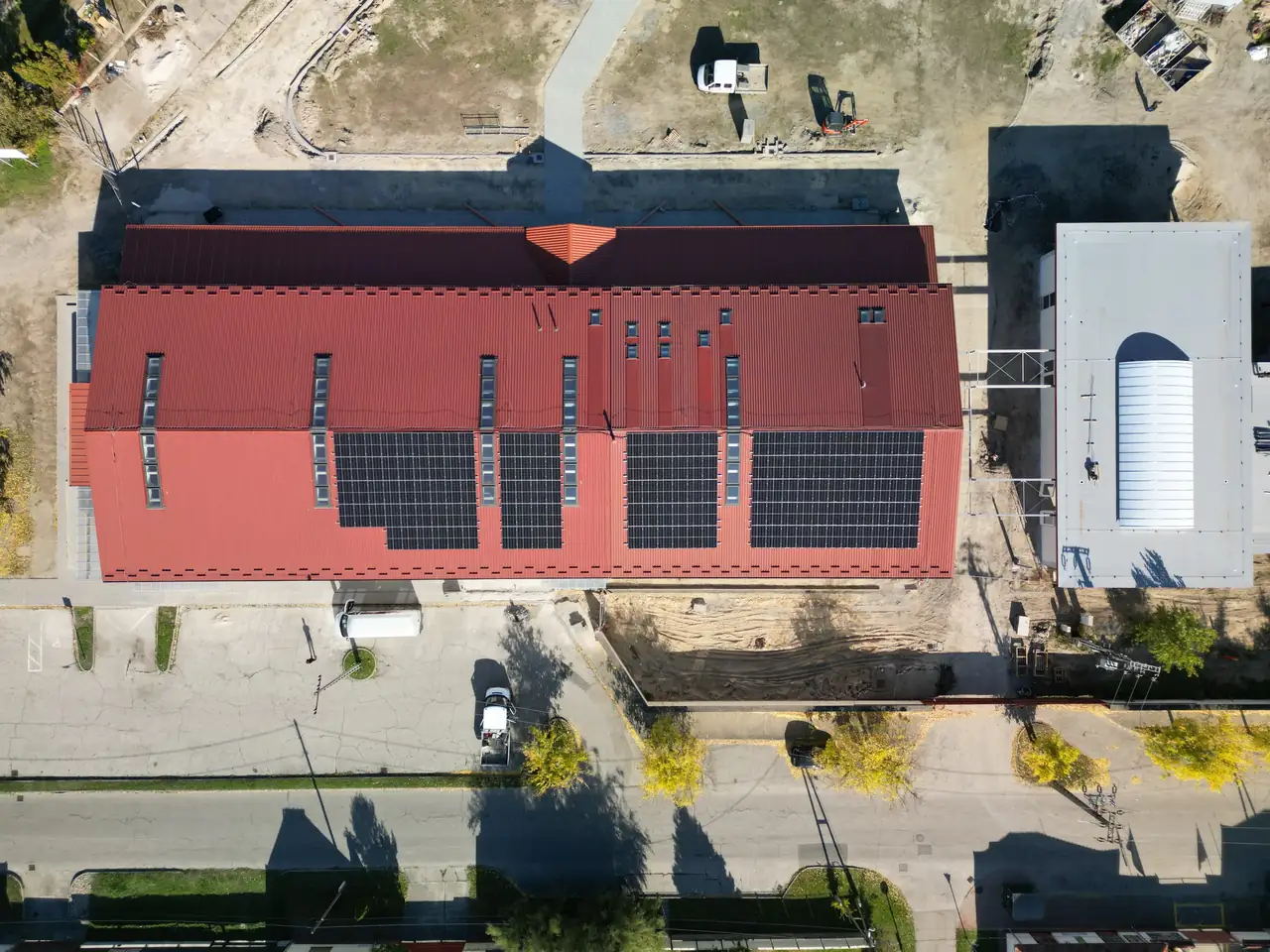 Dóc településén az Ares Solar Construction Kft. által végzett napelem telepítés látható egy piros tetőn. Az épület tetején több napelem panelek sorakoznak, amelyeket a napfény optimális kihasználására terveztek. Az alábbi területen teherautók és járművek parkolnak, míg a környezet rendezett és jól karbantartott. A telepítés célja a fenntartható energiaforrások kihasználása.