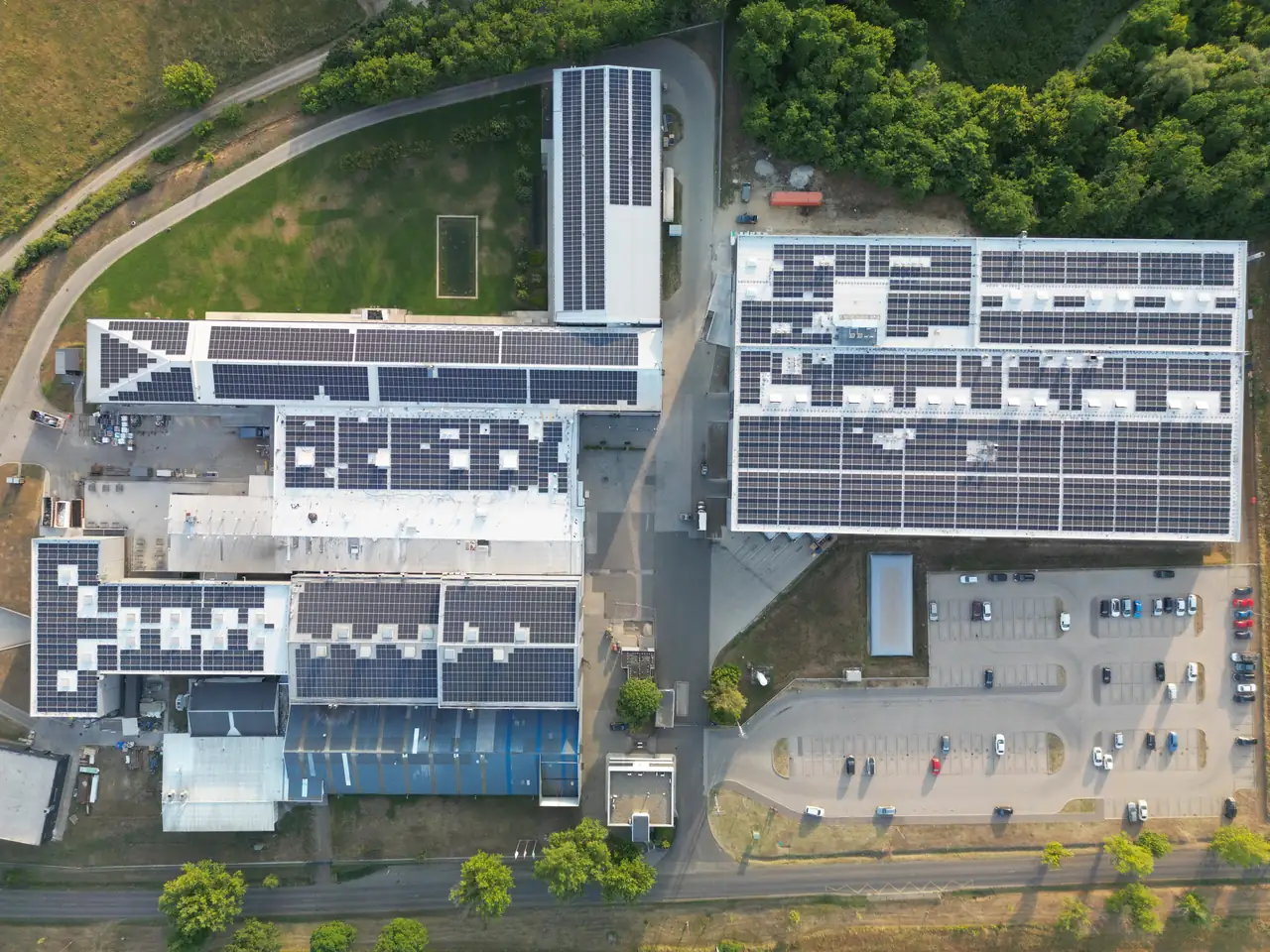 Légi felvétel Hajdúszoboszlóról, ahol az Ares Solar Construction Kft. napelem telepítési projektje látható. Az épület tetején elhelyezett napelemek sorakoznak, amelyek a környező zöld területekkel együtt mutatják a fenntartható energiaforrások használatának fontosságát. A kép jól szemlélteti a modern napelem rendszerek integrálását ipari épületekbe.