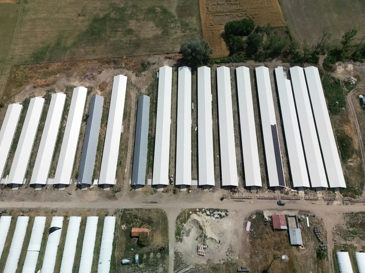 A képen Dóc városában található napelemes rendszerek telepítésének folyamata látható, ahol az Ares Solar Construction Kft. által telepített napelemek szépen elhelyezkednek a mezőgazdasági épületek tetején. Az épületek hosszú sorokban helyezkednek el, a környező terület zöldellő mezőkkel és földutakkal van körülvéve, ami a napelem telepítés modern megoldásait tükrözi.