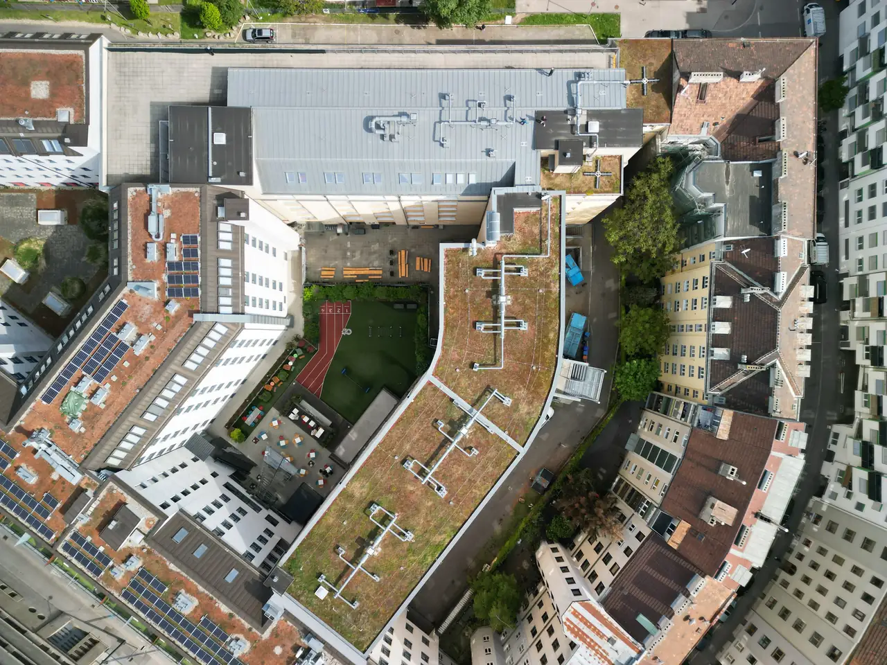 Kaposvár városában, az Ares Solar Construction Kft. napelem telepítési projektjének légifelvétele látható. Az épületek tetején elhelyezett napelemek jól láthatók, amelyek körül zöld tetők és teraszok találhatók. A kép bemutatja a modern városi építészet és a fenntartható energia használatának összhangját Kaposváron, ahol a napelem telepítése egyre népszerűbb megoldás.