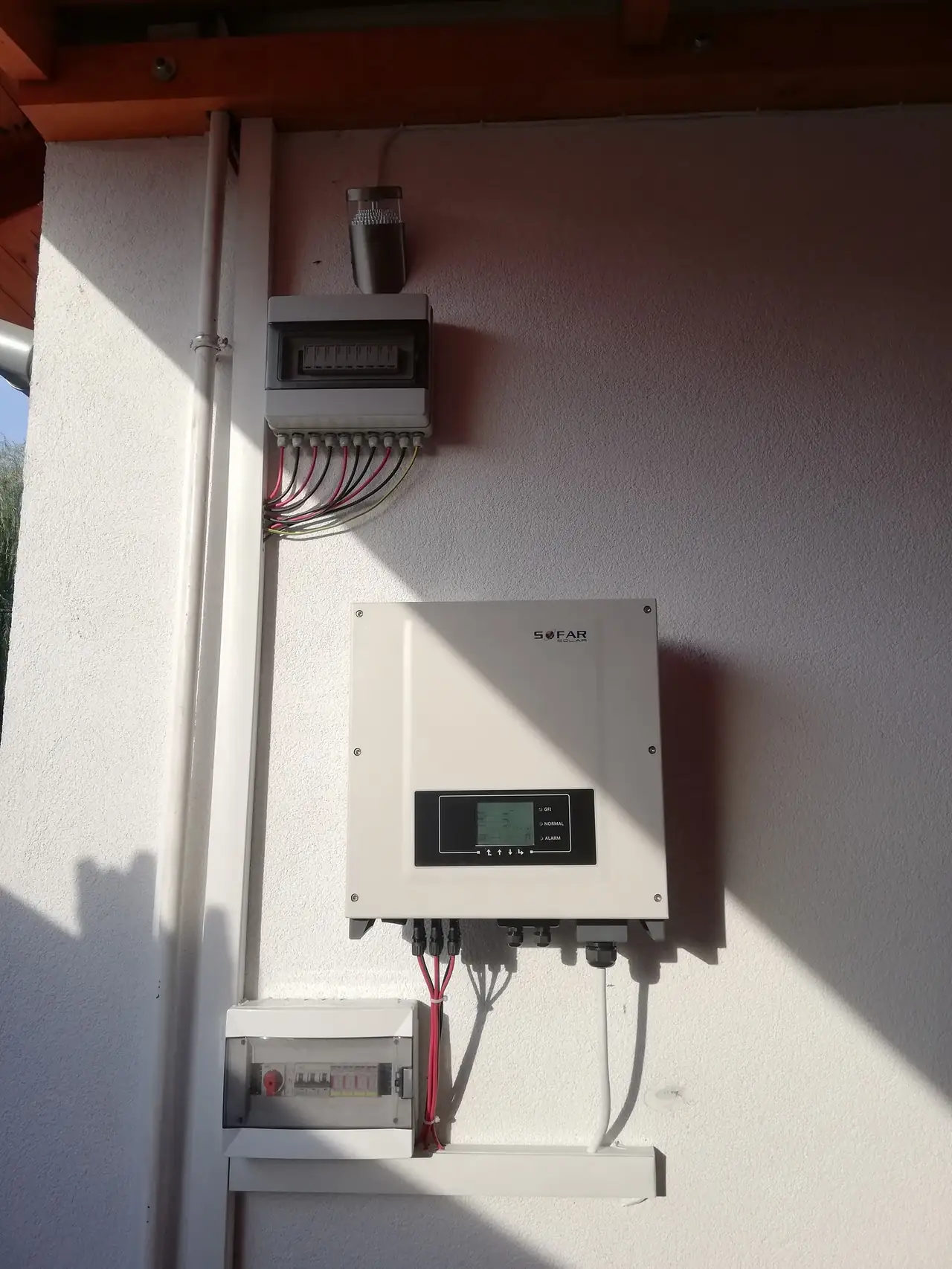 Baja városában, az Ares Solar Construction Kft. napelem telepítési projektje során készült kép, amelyen egy napelemes inverter látható a falra szerelve. Az inverter mellett egy elosztópanel és különböző kábelek találhatóak, amelyek a napelemes rendszer működéséhez szükségesek. A kép jól szemlélteti a napelem telepítés technikai részleteit és a szakértelmet, amit a cég képvisel.