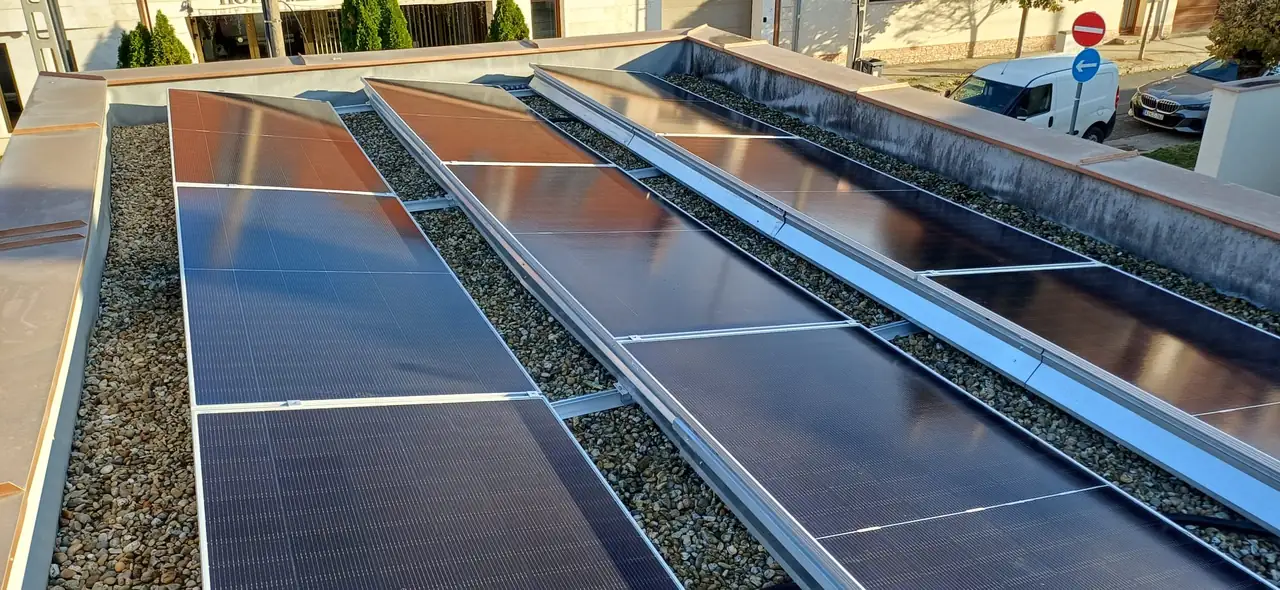 A képen a Kecskeméten, az Ares Solar Construction Kft. által telepített napelemek láthatók egy tetőn. A napelemek sorokban helyezkednek el, sima felületük tükrözi a napfényt. A környezetben láthatóak a város utcái, és a telepítéshez szükséges technikai elemek is. A napelem telepítés modern megoldásokat képvisel a fenntartható energiahasználat érdekében.